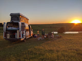 RV rental adventure! Family enjoys a scenic sunset campout with their pop-top camper van by a pond.