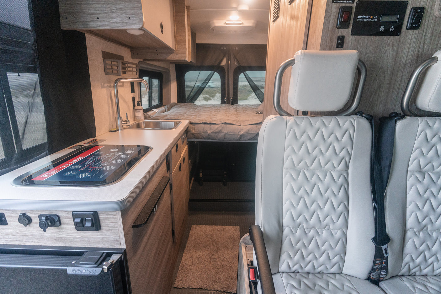 Modern rv rental interior: compact kitchen, rear bed, and passenger seating, plus a solar charge controller panel.