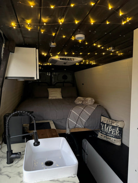Step inside this cozy rv rental van! Enjoy the inviting bed, warm string lights, and functional kitchen with sink & faucet.