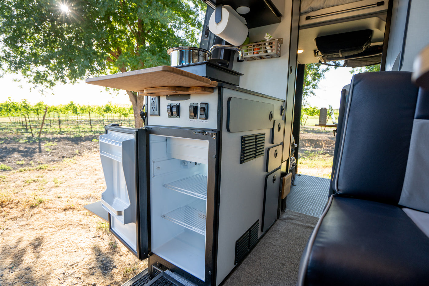 RV rental: Interior kitchen with open refrigerator, sink, and cooking area, overlooking a vineyard.