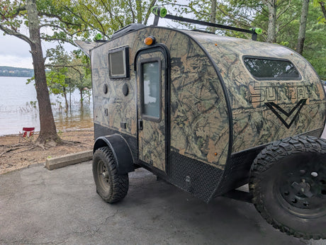 This Sport Sunray camouflage RV rental, perfect for outdoor camping adventures, is parked lakeside.