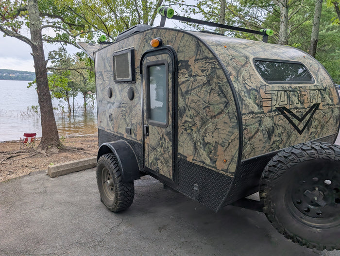 This Sport Sunray camouflage RV rental, perfect for outdoor camping adventures, is parked lakeside.