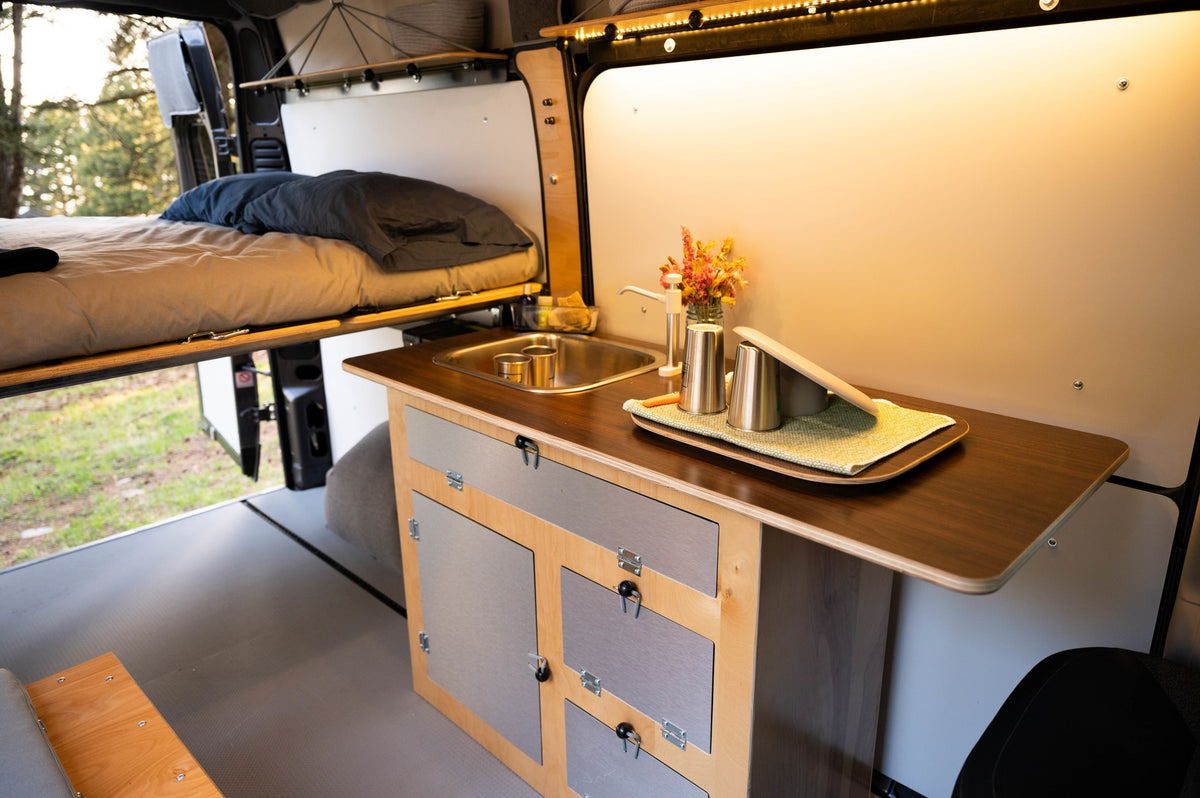 Inside this rv rental, a compact kitchen with a sink and storage is shown, next to a comfy raised bed. — photo 8
