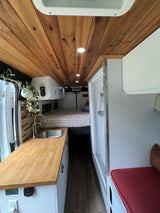 This RV rental interior boasts a beautifully crafted wooden ceiling, compact kitchen, comfy bed, and a built-in shower.