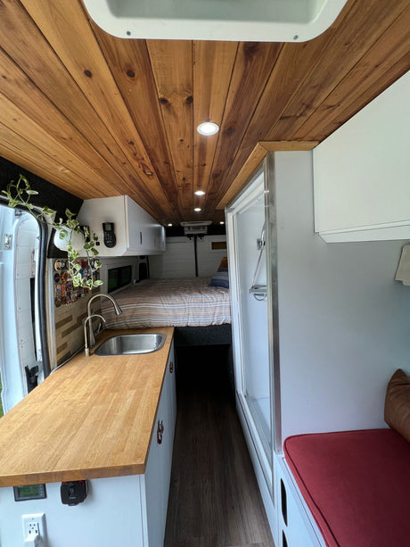This RV rental interior boasts a beautifully crafted wooden ceiling, compact kitchen, comfy bed, and a built-in shower.
