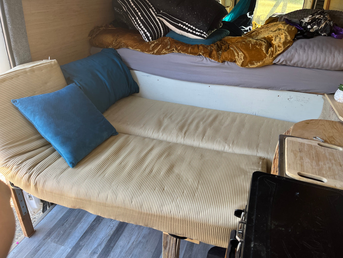 This RV rental shows a cozy, multi-functional interior with a ribbed sofa-bed, elevated sleeping area, and small kitchen space.