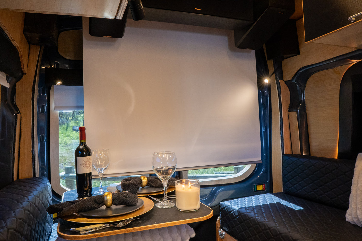 Cozy RV rental van interior featuring a dining table set with wine, a lit candle, and speakers for an intimate evening.
