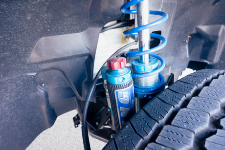 RV rental's robust off-road suspension system shown: a blue coilover shock and an external reservoir, beside a tire.