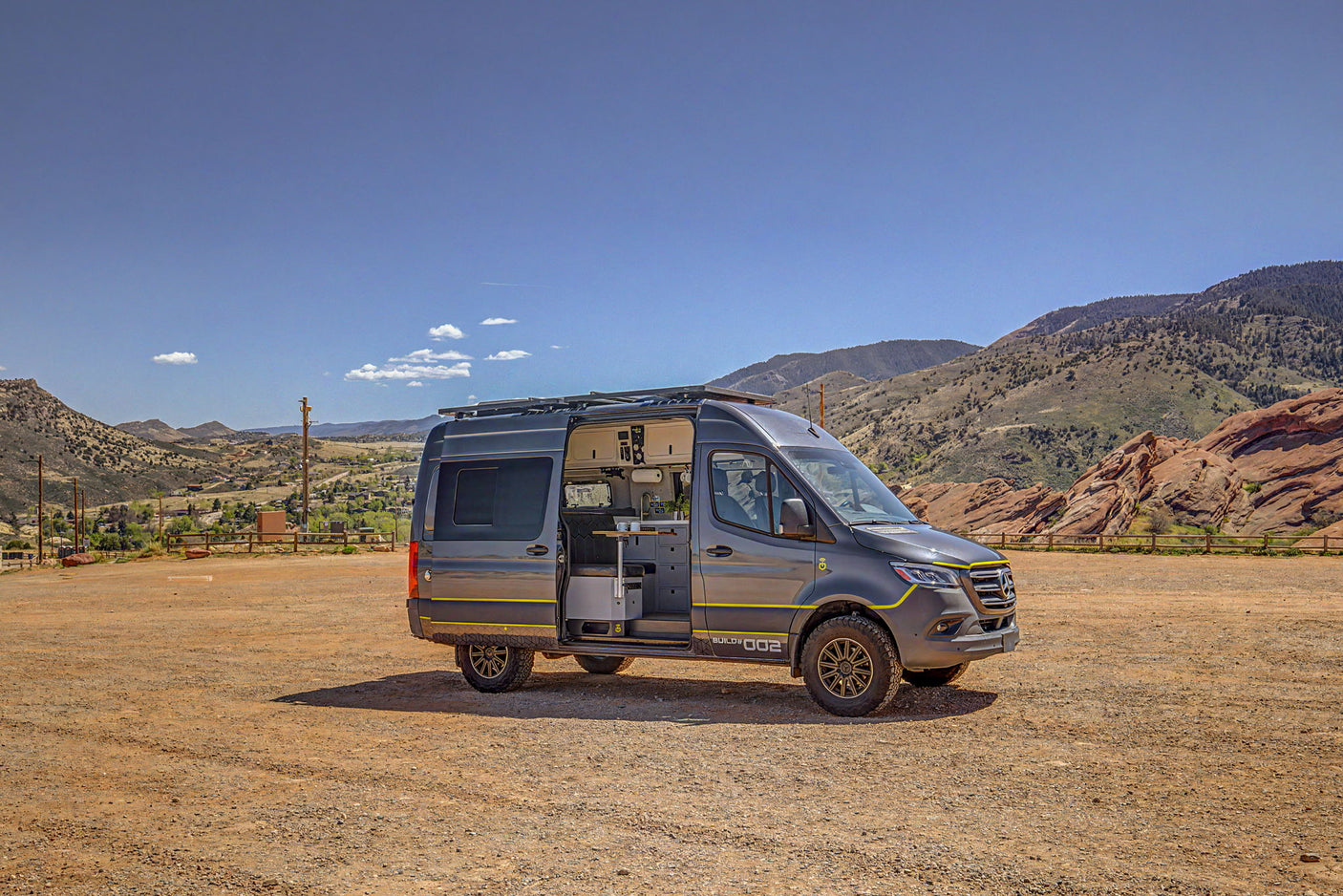 A custom gray Mercedes Sprinter camper van, available for rv rental, parked on a dirt lot with scenic mountains and valleys.