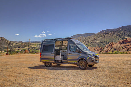 A custom gray Mercedes Sprinter camper van, available for rv rental, parked on a dirt lot with scenic mountains and valleys.