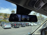 View from RV rental: Dashcam mirror shows parking lot with cars, distant houses, and interior cabin details.