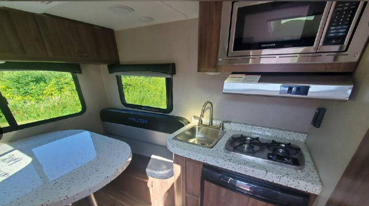 Compact RV rental interior featuring a kitchen with sink, stove, microwave, and a dining area with scenic window views.