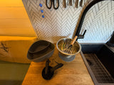RV rental kitchen: wooden counter with black sink & faucet, herringbone backsplash, and cooking essentials like a colander, bowl, and measuring cups.