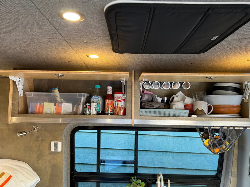 Well-organized RV rental living space: overhead cabinets stocked with kitchen essentials, bedding, and window view. — photo 18