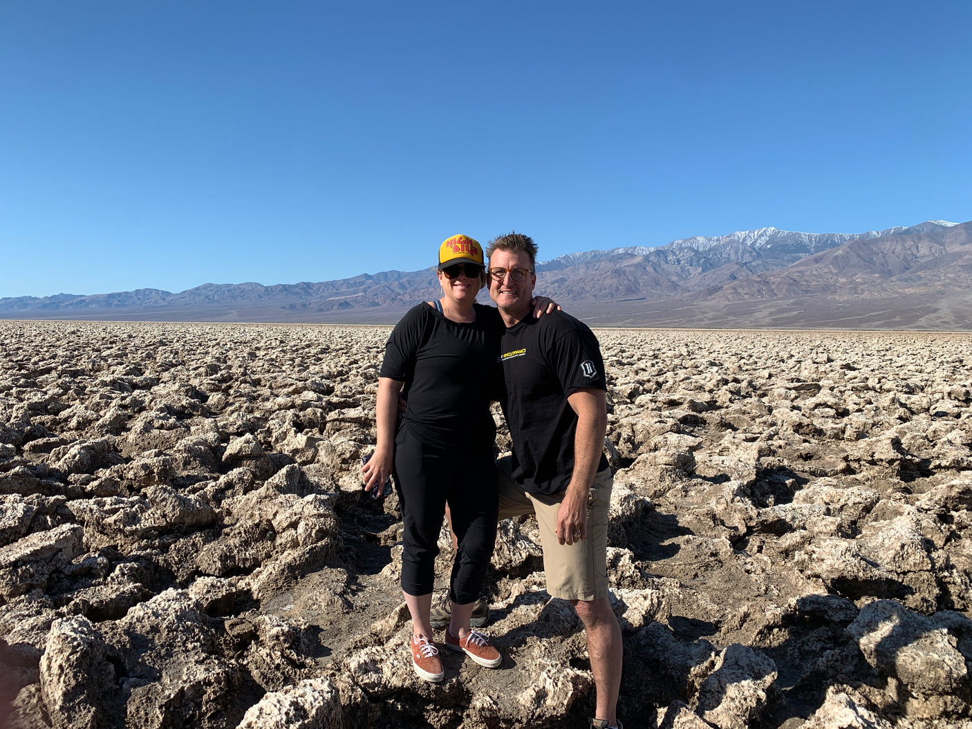 Couple smiles in a scenic desert landscape with unique rocky terrain and distant mountains, ideal for an RV rental adventure.