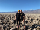 Couple smiles in a scenic desert landscape with unique rocky terrain and distant mountains, ideal for an RV rental adventure.