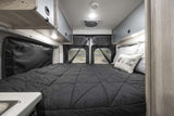 Spacious and comfortable RV rental bedroom with a large bed, overhead storage, and scenic rear door view. Ready for travel!