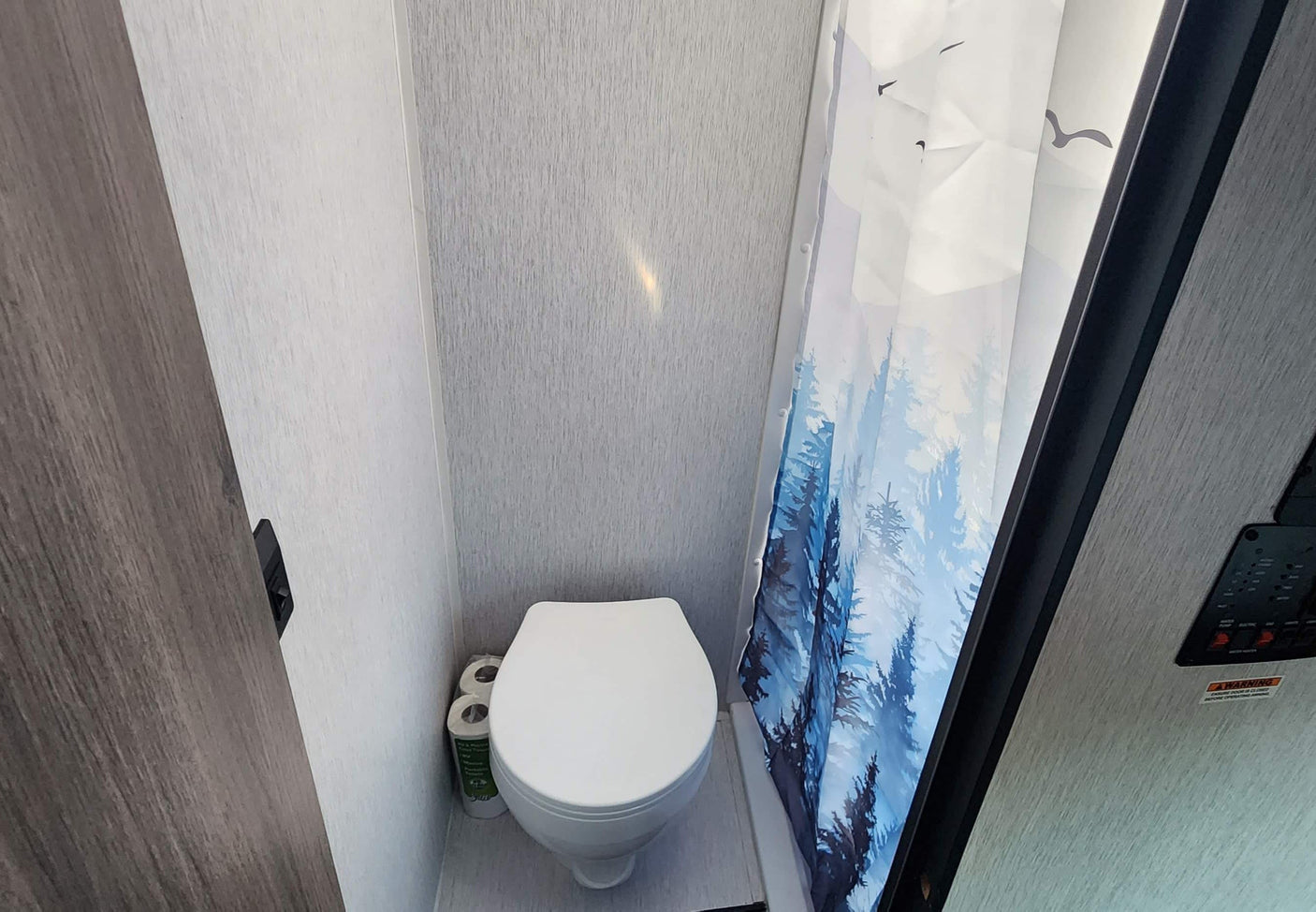 Compact RV rental bathroom with toilet and a blue forest and bird shower curtain. Perfect for on-the-go living.