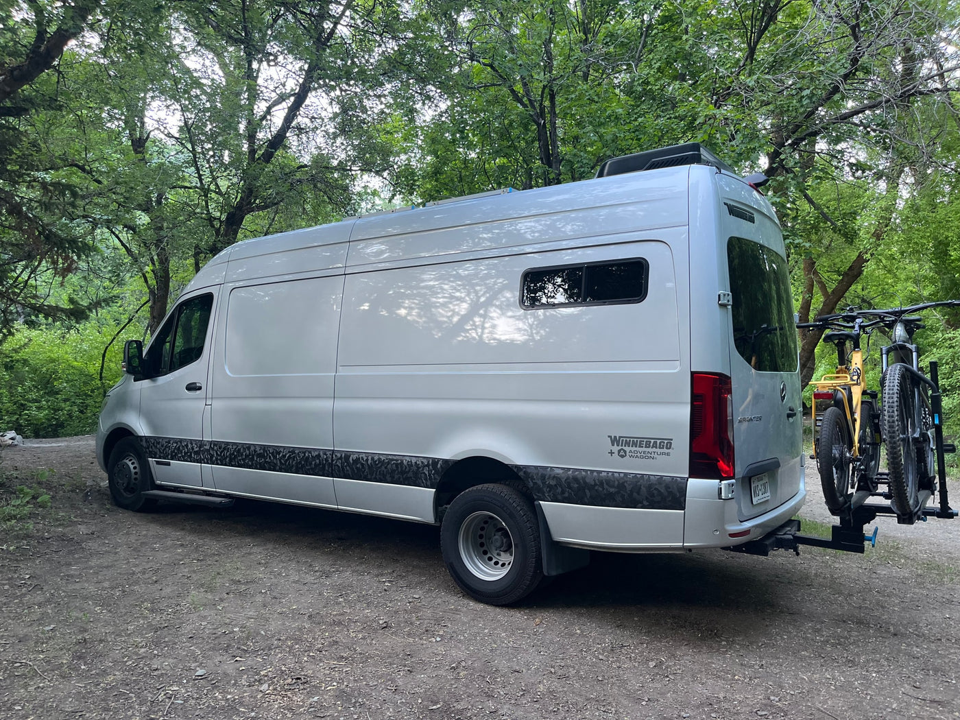 Silver Winnebago Adventure Wagon rv rental van with bikes on rack, parked in a green forest. Perfect for outdoor trips. — photo 17