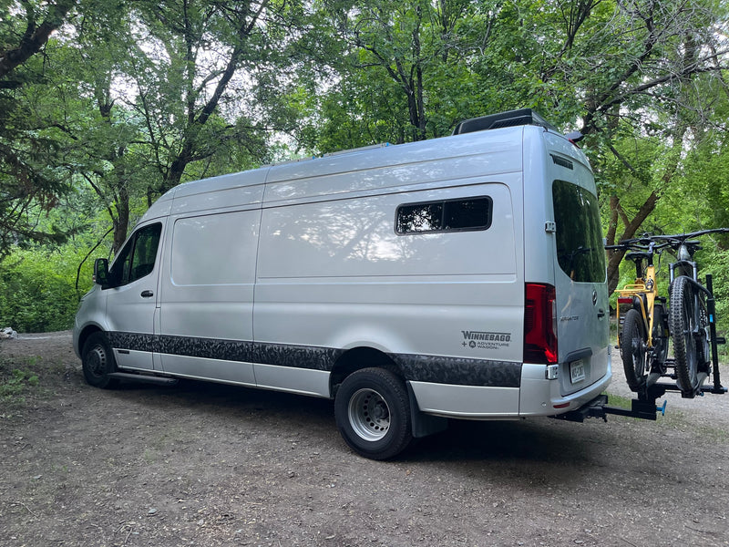 Silver Winnebago Adventure Wagon rv rental van with bikes on rack, parked in a green forest. Perfect for outdoor trips. — photo 17
