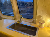 Inside an RV rental: compact kitchen featuring a sink and Trader Joe's hand soap, with a rainy view outside.