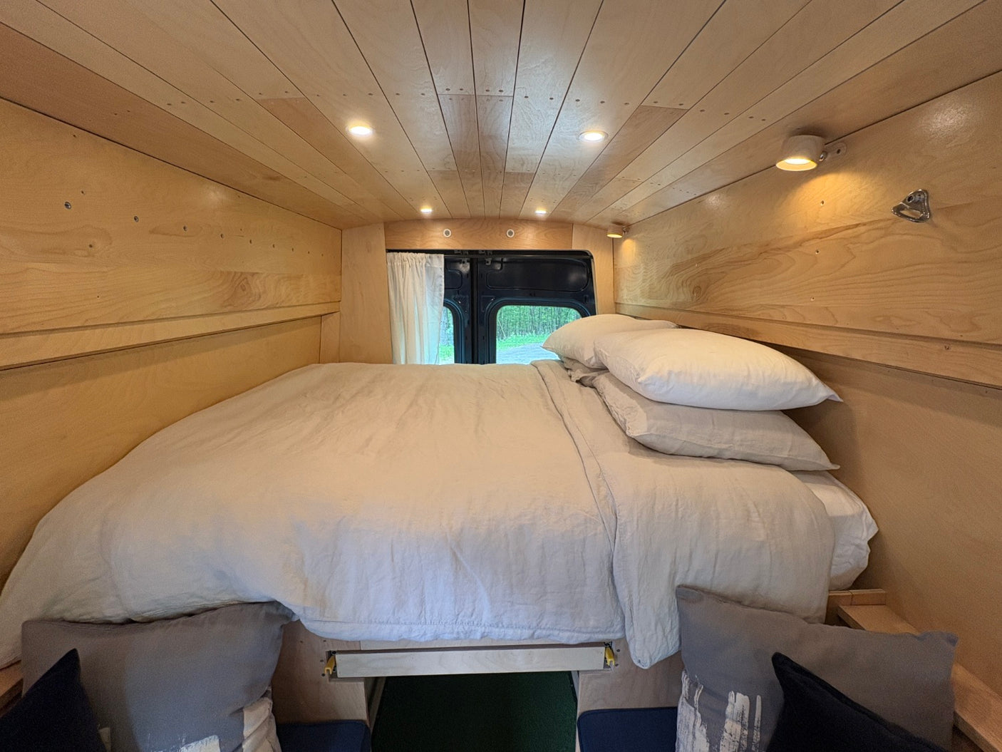 RV rental's cozy camper van interior: a comfortable bed, light wood paneling, and ambient lighting, ready for adventure.