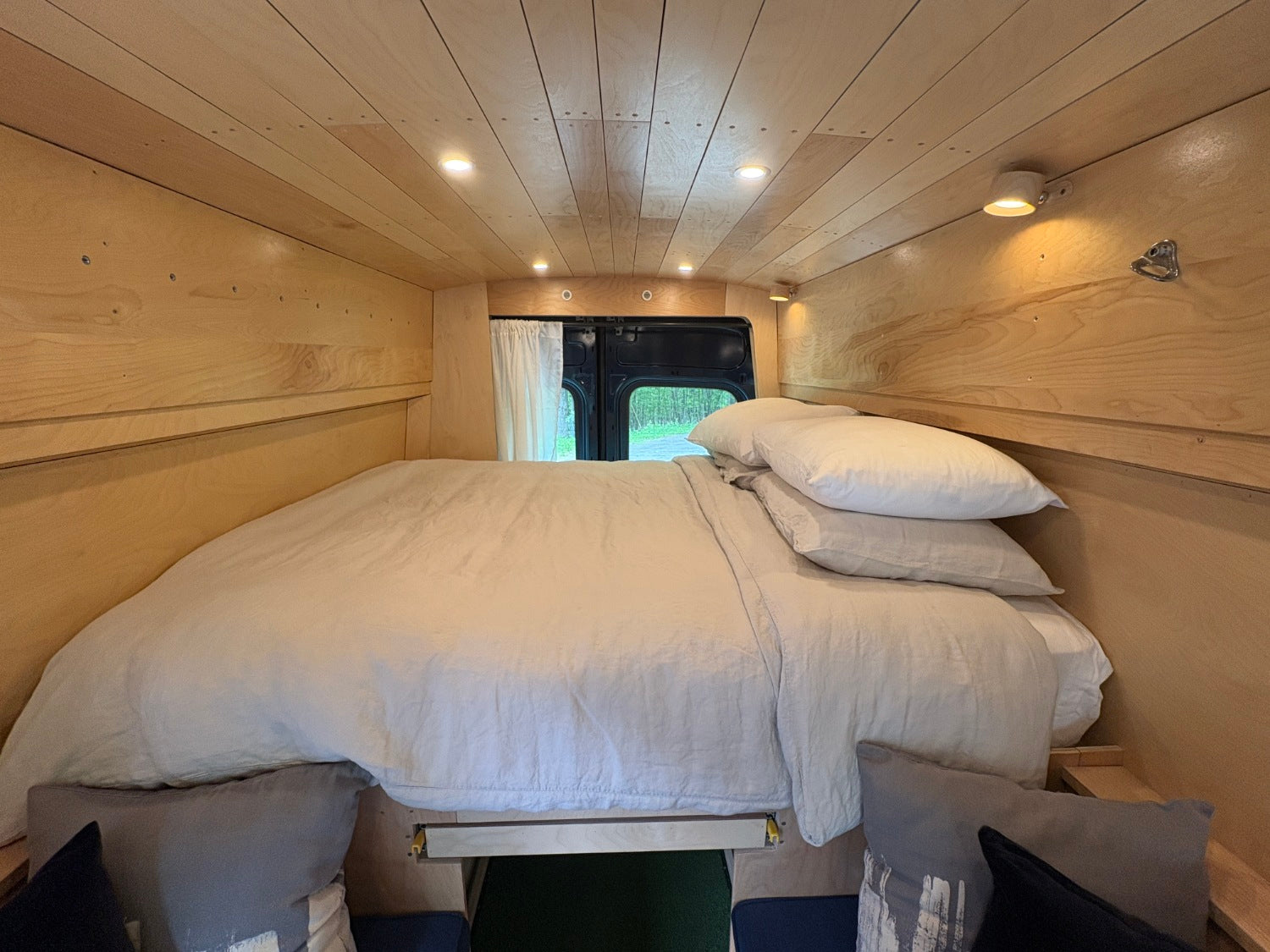 RV rental's cozy camper van interior: a comfortable bed, light wood paneling, and ambient lighting, ready for adventure.