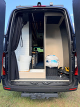 Rear view of an rv rental camper van interior, featuring a tiled shower with portable toilet and organized storage space.