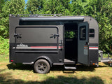Dark grey InTech teardrop camper trailer with an open door, Thule awning, and rugged tires, great for an RV rental.