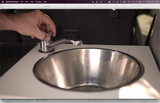 A hand turns a compact faucet at a small stainless steel sink, illustrating a practical amenity in an RV rental.