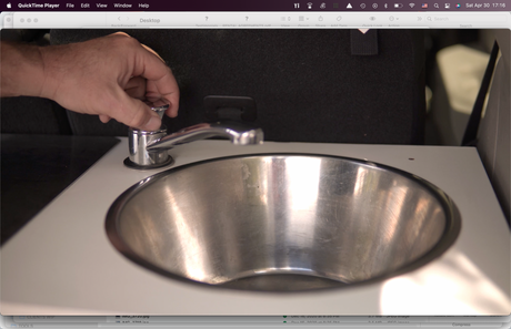 A hand turns a compact faucet at a small stainless steel sink, illustrating a practical amenity in an RV rental.