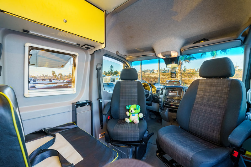 Interior of a bright RV rental, showing the front cabin seats, a cozy living area, and scenic palm tree views. — photo 14
