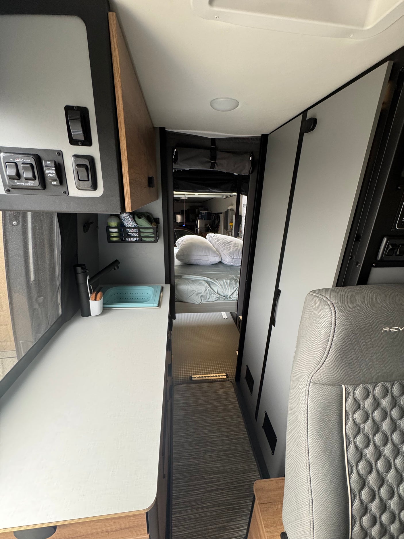 RV rental interior: A compact camper van with a modern kitchen counter, sink, control panel, and a bed visible at the end of the narrow hallway.