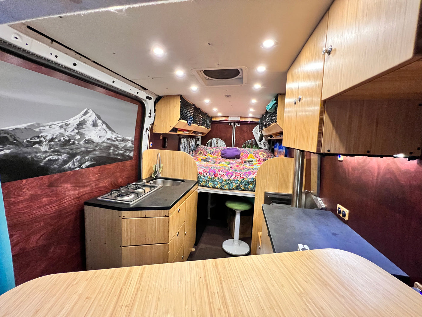 Inside a vibrant **RV rental**: a compact kitchen, colorful bed, ample storage, and a mountain mural. Ready for travel!