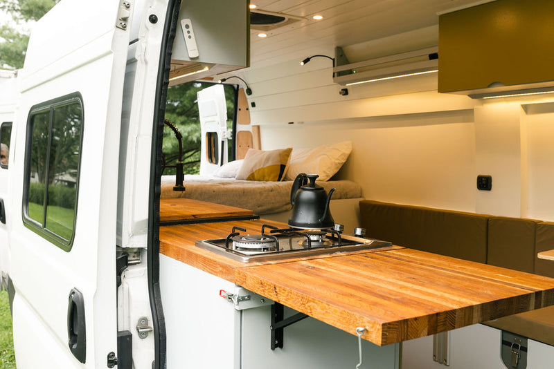 Inside a spacious RV rental camper van, featuring a bright, cozy interior with a wood kitchen counter, stove, bed, and seating. — photo 13