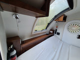 Cozy RV rental interior: a compact bedroom features a bed, wooden storage, a large window, and essential controls.