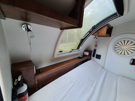 Cozy RV rental interior: a compact bedroom features a bed, wooden storage, a large window, and essential controls.