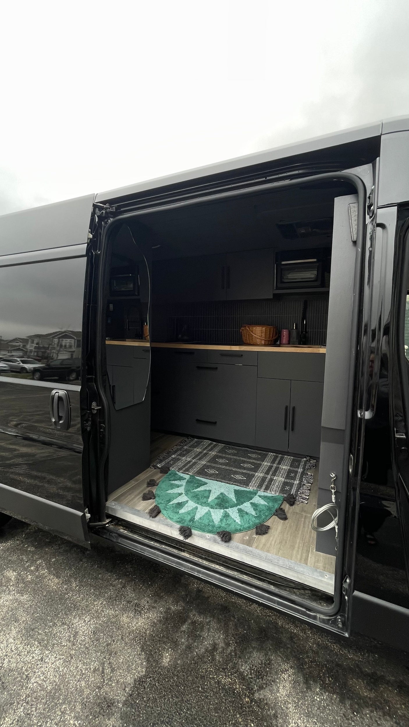 Step inside this modern black RV rental! It features a sleek mobile kitchen with dark cabinets, wood counters, and cozy rugs.