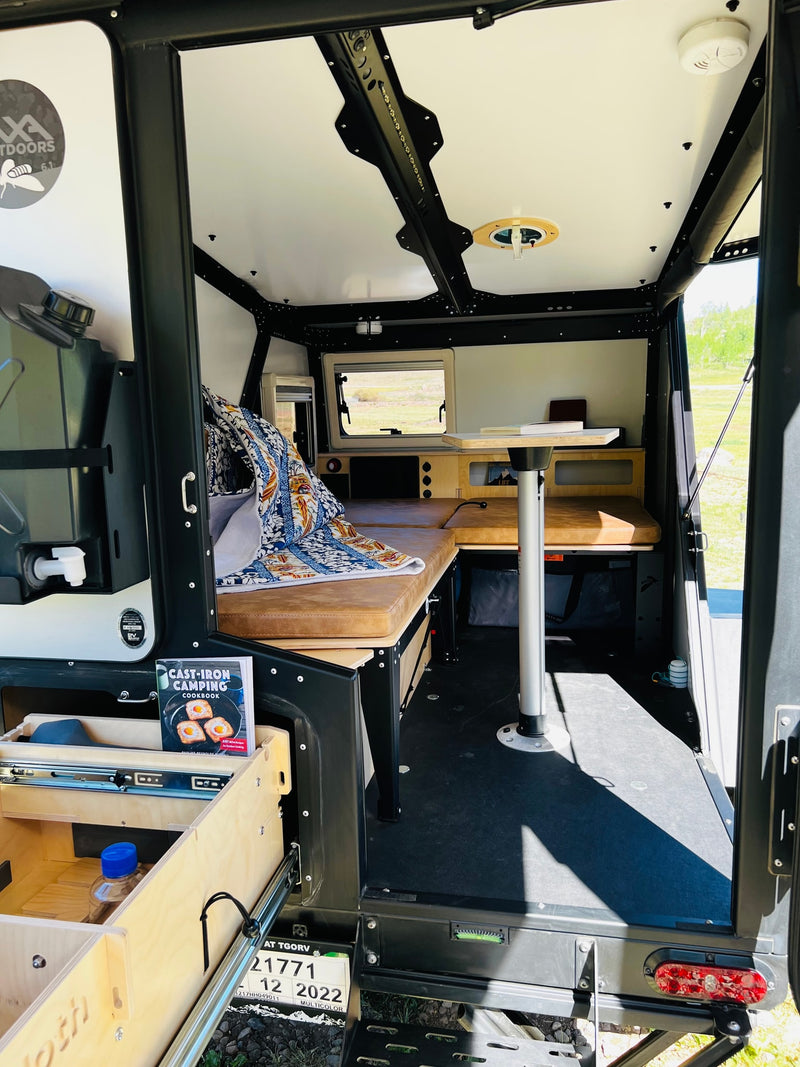 This RV rental interior features a cozy bed, movable table, and pull-out kitchen drawers, ready for camping adventures. — photo 10