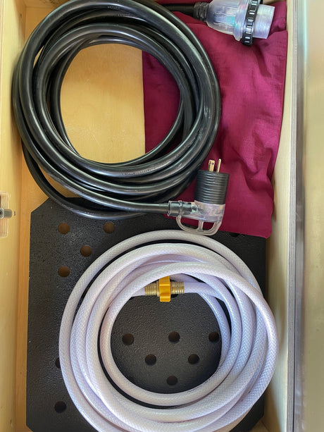 RV rental prep: neatly stored black power cord, clear plug, and white fresh water hose in a compartment.
