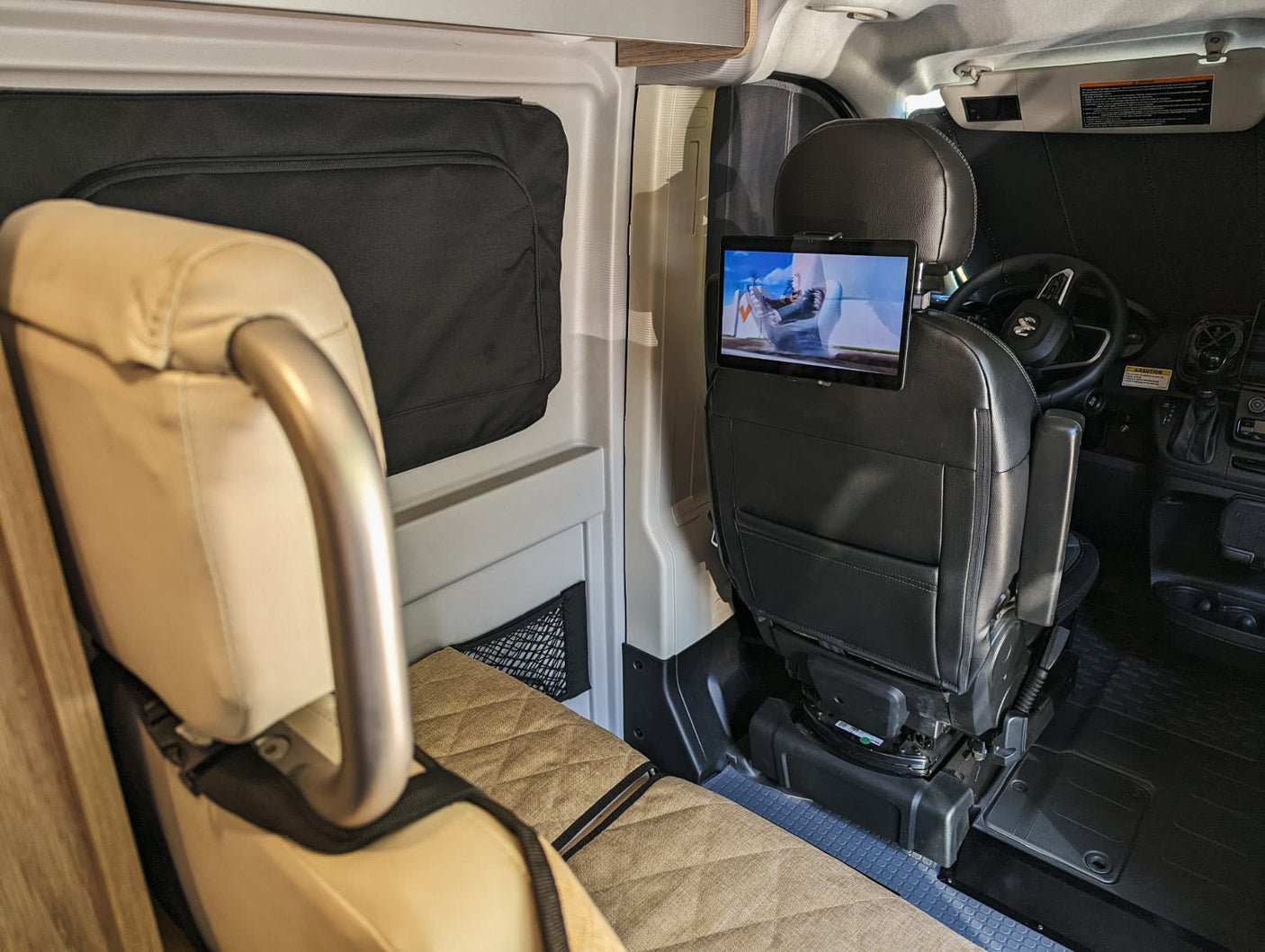 RV rental interior shows a swiveling passenger seat with tablet entertainment, facing a cozy rear bench. Perfect for mobile living.