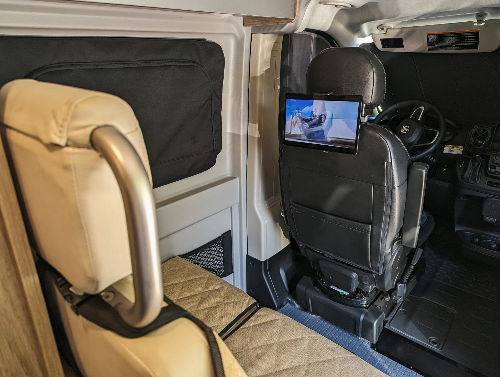 RV rental interior shows a swiveling passenger seat with tablet entertainment, facing a cozy rear bench. Perfect for mobile living.