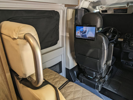 RV rental interior shows a swiveling passenger seat with tablet entertainment, facing a cozy rear bench. Perfect for mobile living.
