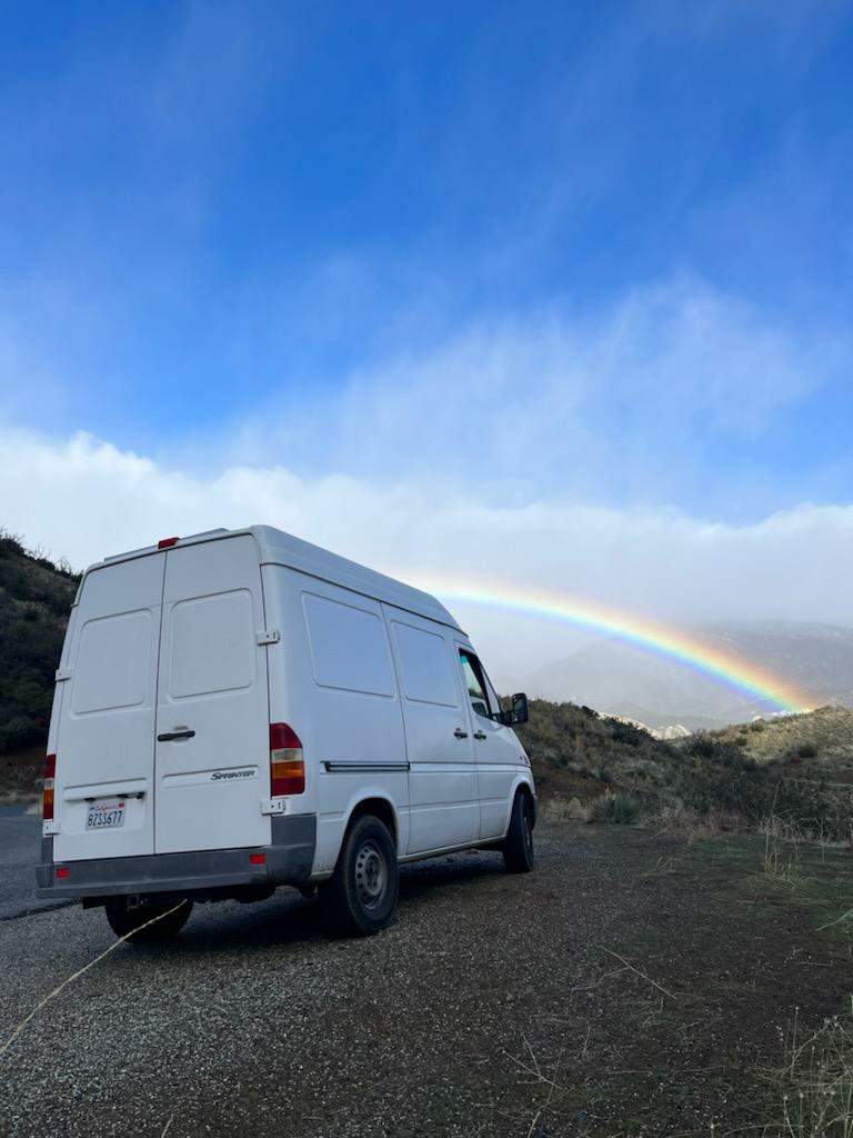  a person with a hat and fleece explores custom wood drawers and shelves in their mobile home.|A man in a green beanie takes a selfie with a woman inside their white rv rental van — photo 6