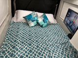 This RV rental features a cozy bed with a teal blanket, patterned pillows, & a TV playing Minions for a relaxing stay.