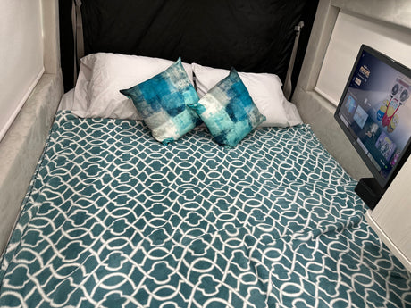 This RV rental features a cozy bed with a teal blanket, patterned pillows, & a TV playing Minions for a relaxing stay.