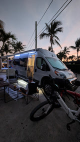 A cozy RV rental camper van scene at dusk, with palm trees, outdoor seating, and Sondors e-bikes. Perfect for travelers.