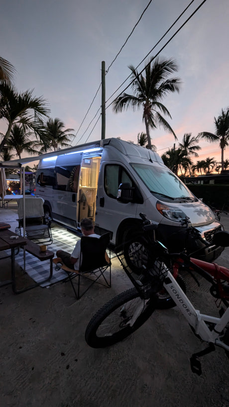 A cozy RV rental camper van scene at dusk, with palm trees, outdoor seating, and Sondors e-bikes. Perfect for travelers.
