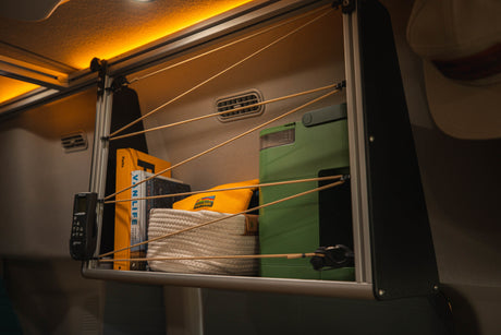 Optimized RV rental storage: a shelving unit with books, a basket, and gear, secured by elastic cords, under warm LED light.