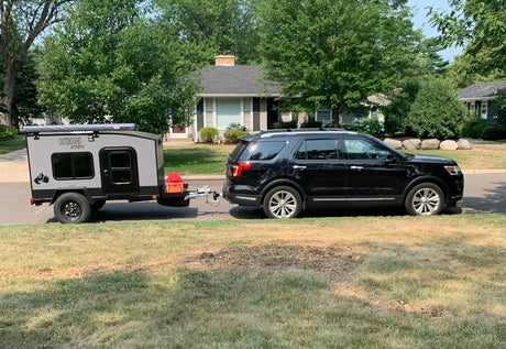 A black SUV tows a gray 'Outbound Extreme' camper trailer, parked on a suburban street. Ideal for an RV rental getaway.